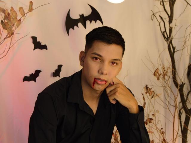 EdwinBlaze with dark hair, black shirt, and blood on his chin, biting his finger, with bat cutouts and dry branches in the background, looking sexy and mysterious.