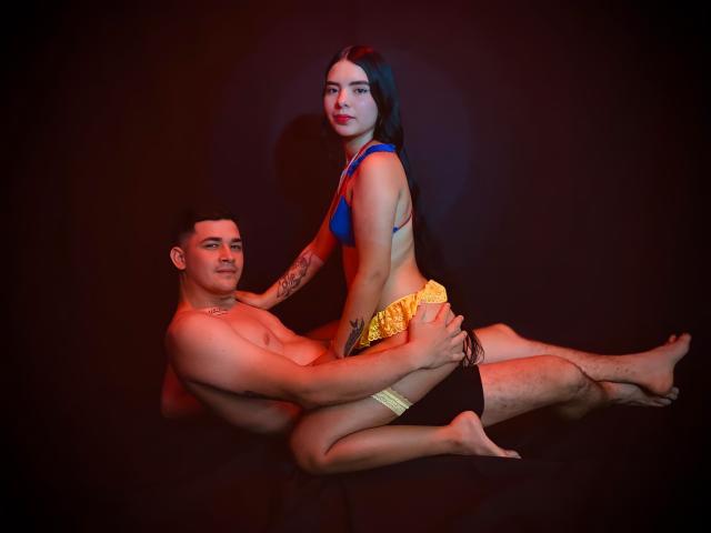 Laura e Kevin, com seios em um sutiã azul, shorts amarelos, sentadas no rosto nu, musculoso, sem camisa, com detalhes pretos, circuncidado, ereto, com ponta flácida, tatuado, com pernas peludas, cabelo escuro, lábios vermelhos e sorrindo de Kevin..
