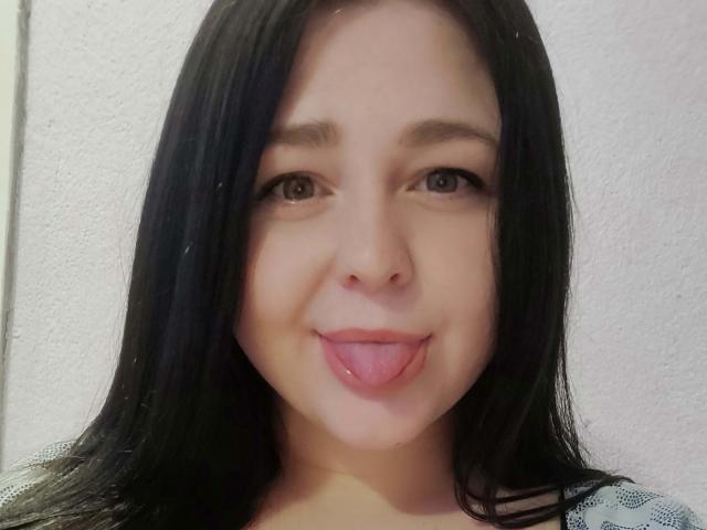 EricaLaLovely has black hair, brown eyes, and a cute face with her tongue sticking out. She's looking straight at the camera with a playful expression.