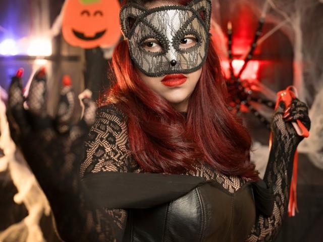 MorganMoretz with red hair, black lace mask, red lipstick, lace gloves, black leather top, holding red whip, showing black lace-covered tits, sexy, Halloween costume, dark background.