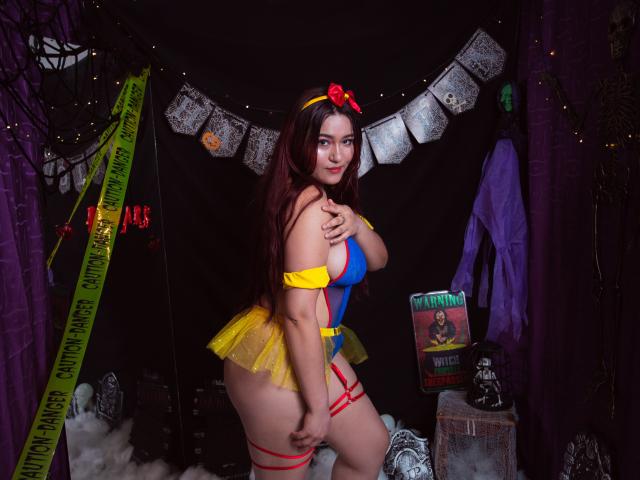 MaddieMoon in einem sexy Schneewittchen-Cosplay mit gelbem Tüll, einem blauen Oberteil, roten Trägern und einer roten Schleife, die ihr großes Hintern und ihre prallen Brüste zeigt, mit einem verführerischen Lächeln..