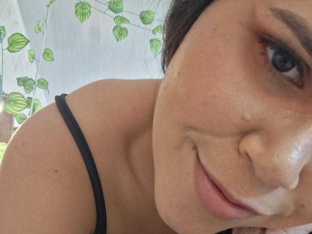 Il viso di DanTaylor, con un leggero sorriso, occhi marroni, una spallina sottile nera e spalle scoperte. La sua pelle ha qualche piccola lentiggine e un leggero alone..