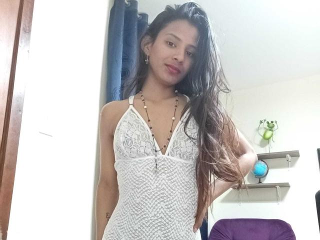 AriVelvet with long brown hair, wearing a white lace halter dress, standing, hand in hair, slight smile, necklace, small tits, cute, bedroom, purple chair, blue curtain.