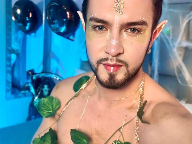 DaltonWhite zonder shirt, met groene schmink op zijn gezicht, een gouden ketting en een wijnrank over zijn borst, heeft een rode stip op zijn neus en een bloem op zijn voorhoofd. Elfachtige oren..