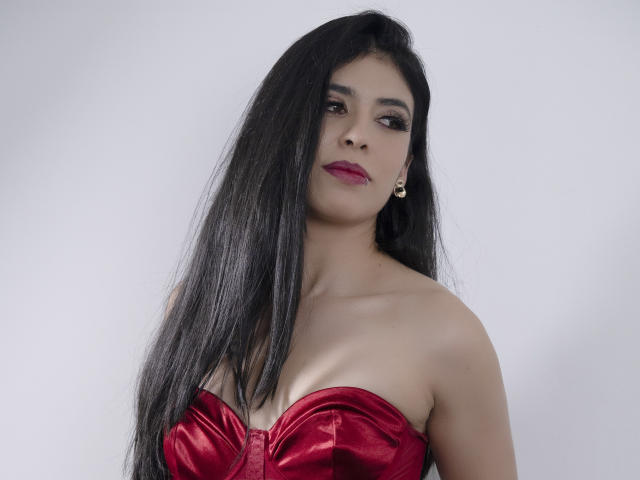 MiluSky with long black hair, red satin strapless top showing her boobs, red lipstick, and small gold earrings, looking slightly to the side.