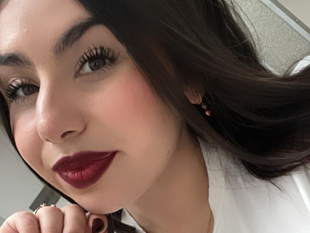 VenusxMusa ha la pelle chiara, i capelli castano scuro, le sopracciglia folte, il rossetto rosso e le lunghe ciglia. Sorride con una mano vicino al viso, indossando una camicia bianca..