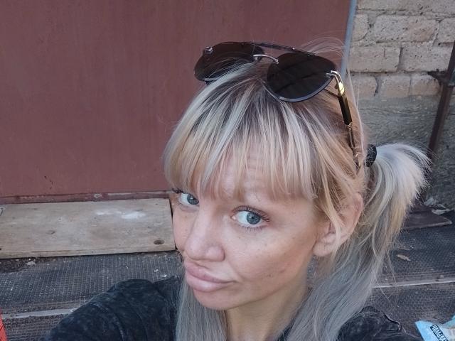CamileRay has blonde pigtails, blue eyes, and sunglasses on her head. She's pouting with a slight smirk, wearing a dark shirt. Her nose is slightly freckled.