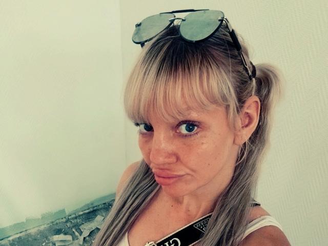 CamileRay has blonde pigtails, blue eyes, and wears sunglasses on her head. She's looking at the camera with a slight pout, wearing a white tank top.