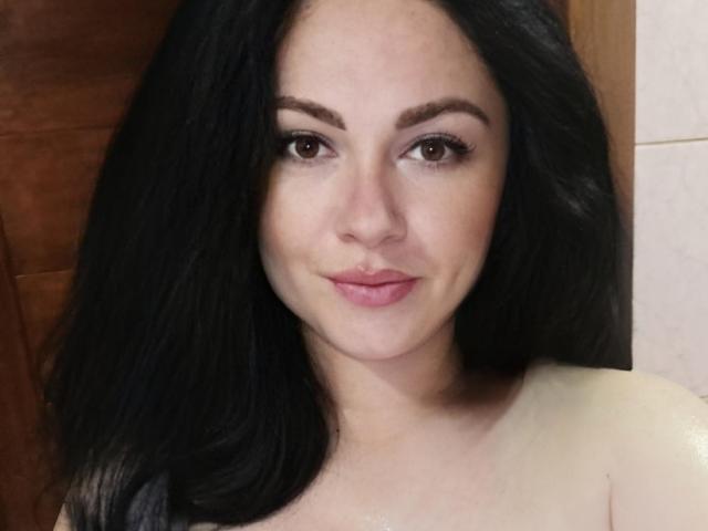 FortuneHelena has medium-sized tits, dark wavy hair, and a cute smile with pink lips, looking straight at the camera with brown eyes.
