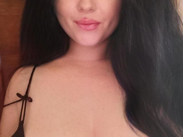 Fortune : Helena, avec son rouge à lèvres rose, ses cheveux noirs et son sourire discret. Elle porte un bandeau noir, qui révèle ses seins volumineux et doux, ainsi que sa peau claire..