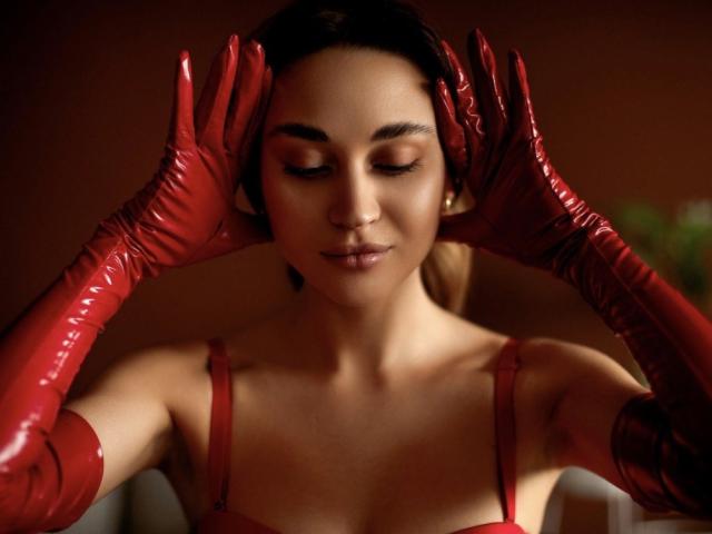 AlexaWilds with red, shiny latex gloves, eyes closed, touching ears, wearing a red bra, soft brown skin, dark hair, subtle smile, calm expression, gentle lighting.