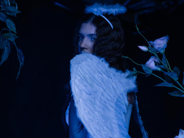 BelleLovely with angel wings, blue eyes, and fluffy halo, looking over shoulder, dark blue light, pink roses on right, white feather wings, wavy brown hair, subtle smile.