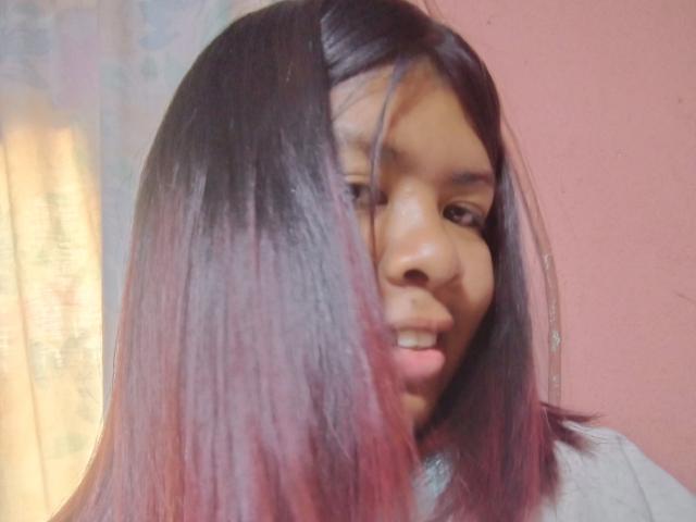 MariahSquirting69 has dark brown, shoulder-length hair with pink tips, and is smiling slightly with a medium skin tone, wearing a gray shirt. Her face is partially obscured.