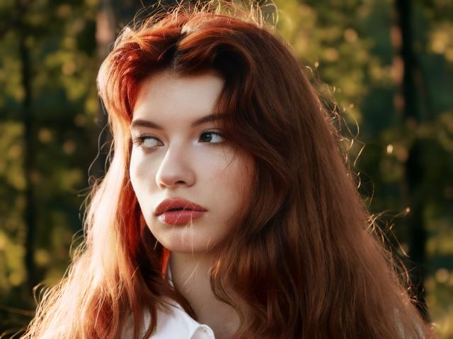LoliyPop has long, wavy red hair and a fair skin tone, with subtle freckles, looking to the side with pouty red lips. Her green eyes are slightly upturned.