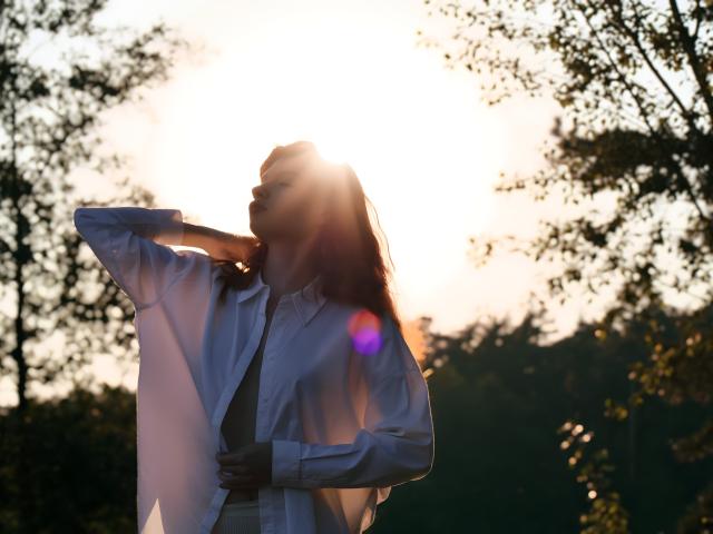LoliyPop with long red hair wearing a white shirt, standing in a forest, looking to the side with a soft smile, holding the shirt's edge. Boobs not visible.