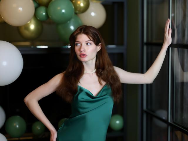 LoliyPop with long brown hair, green eyes, and pale skin wears a green dress, standing with one arm on a window, surrounded by green and white balloons.