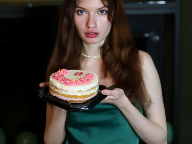 LoliyPop with long brown hair, green dress, and pearl necklace, standing by a window, holding the frame, surrounded by white and green balloons, looking directly at the camera.
