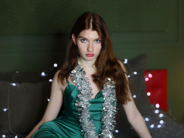LoliyPop with shiny silver tinsel hanging over her green satin dress, showing her boobs and wearing pink lipstick, brown wavy hair, blurred bokeh lights in the background.