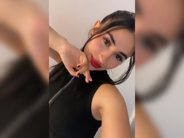 Bubochka, con i suoi lunghi capelli castani, indossa un abito nero con stelle bianche e si trova di fronte a uno specchio rotondo, osservando il suo riflesso e toccando un lavandino grigio in vimini..