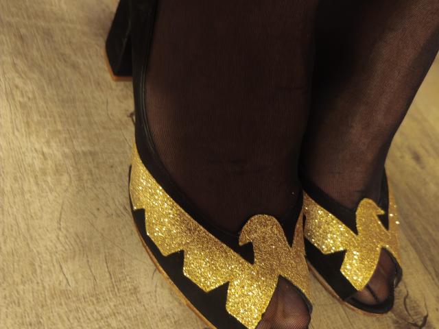 OrianaLaFrancaise's feet in black, sheer stockings with gold, glittery, criss-cross patterned, high-heeled shoes on wooden floor.