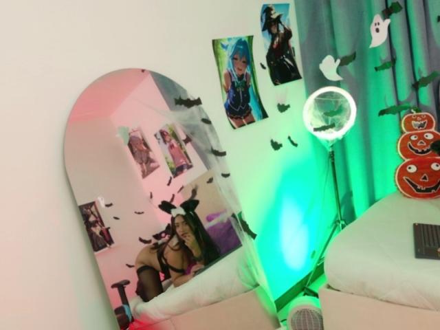 AmmyLewis's room with a snowboard leaning against the wall, decorated with photos, green and pink lights, a ring light, and a curtain with pumpkin faces.