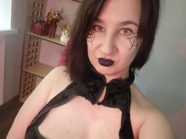GoddessSophie69 with black lipstick, dark eye makeup, and black lace halter top showing her tits. She has pale skin, blue eyes, and short black hair.