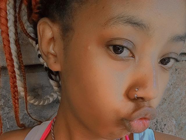 SkyNikey has a brown skin tone, red and white braided hair, and a nose piercing with two silver studs. Pouting with pinkish lips. Visible ear with small black earring.