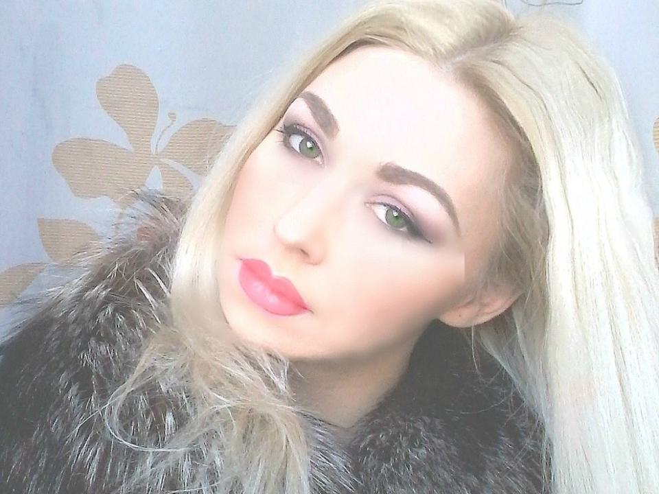 BellaxTorn has blonde hair, green eyes, pink lipstick, and a fur coat. She's looking at the camera with a slight tilt, giving a sexy, sultry vibe.