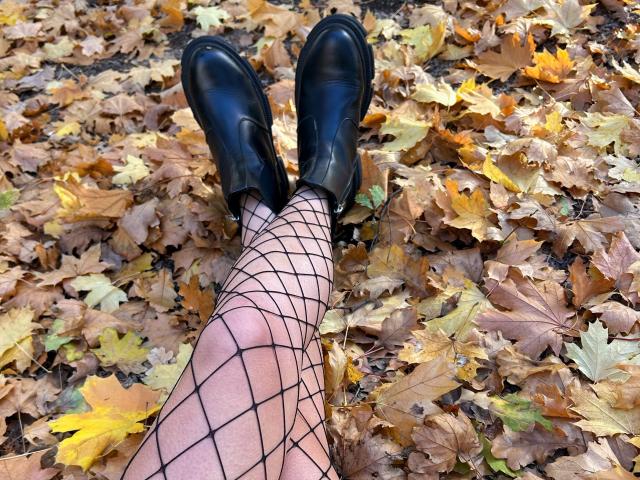 Karish's legs in fishnet stockings, black leather shoes, standing on a bed of yellow and brown autumn leaves.