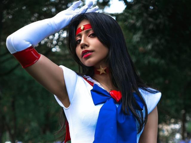 VioletXBloom, a sexy anime girl, with long black hair, wearing a white and blue magical girl outfit, red headband, and white gloves, touches her head, showing her tits.