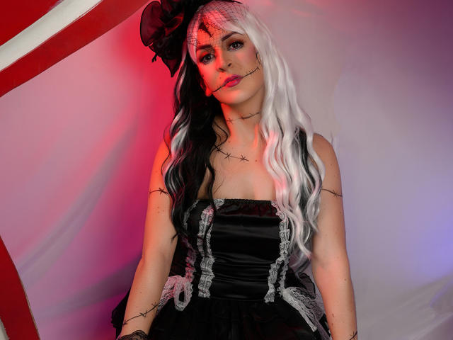 ButtyCherry with black and white wavy hair, black corset, and lace, holding a thorn, has pale skin, red lighting, and a black bow on her head. Boobs visible.