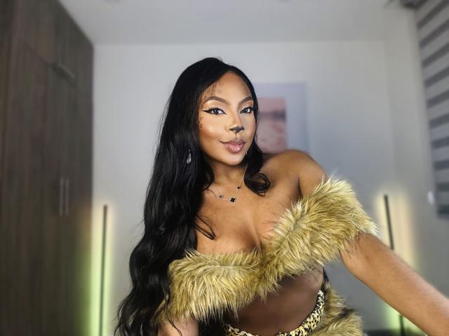 MissMaary with long black hair, wearing a furry off-shoulder top that covers her tits but shows her tan skin and gold necklace. She's smiling with a nose ring.