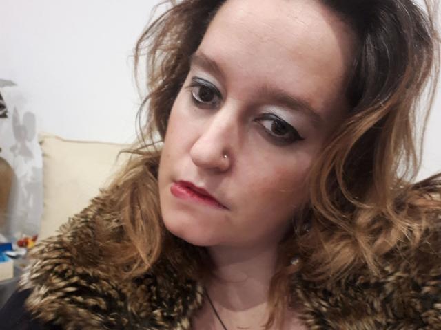 Anita: Roodharig, met golvend bruin haar, een neusring en rode lippenstift, gekleed in een bontgevoerd jasje, met een lichtelijk verveelde uitdrukking, donkere eyeliner en subtiele make-up..