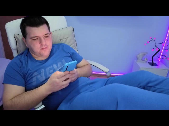 JasonJacks, ein etwas korpulenter Mann, blaues Hemd und Hose, kurzes, dunkles Haar, weißer Stuhl, der auf ein blaues Telefon schaut, entspannt, leicht lächelnd, violettes LED-Licht auf der rechten Seite, ungezwungene Umgebung..