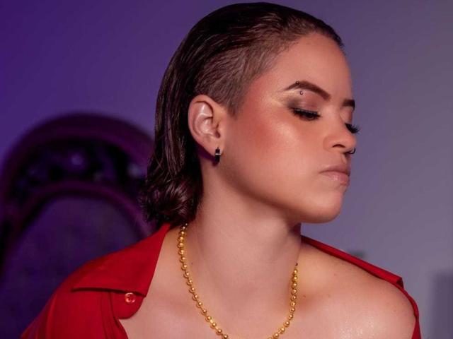 TaylorSexiest with wet brown hair, red shirt, gold chain, and black earrings, eyes closed, showing a small nose piercing and glossy pinkish skin. Boobs partially visible.