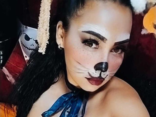 MelanyContrera with cat face makeup, dark lipstick, blue ribbon, black choker, and black hair, looking at camera. She's got tits, freckles, and a cute nose with whiskers.