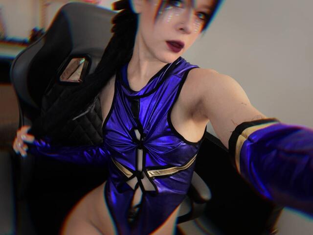 SimaWendy in a shiny purple cosplay outfit, showing her bare tits and side of her ass, taking a selfie with a black chair in the background.