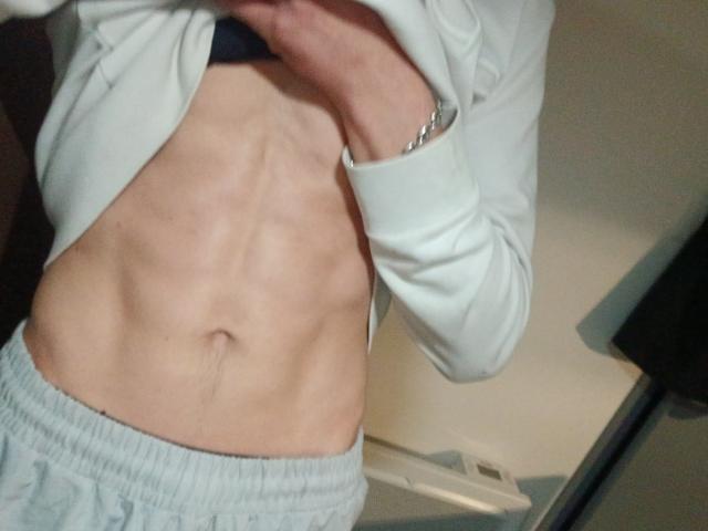 HansX69's flat, muscular abs with visible ribs, wearing light gray sweatpants and a white long-sleeve shirt lifted to expose their torso. HansX69's right wrist has a silver bracelet.