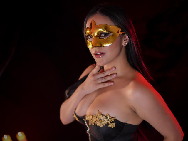 AntonellaWatson with golden mask, black lace corset, and long dark hair, touching her neck, showing her tits, red lighting, and small earrings, looking sexy.