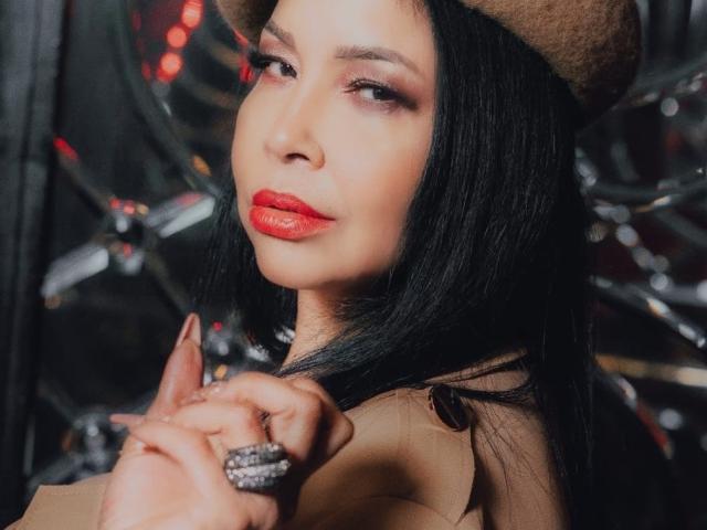 AngelinaDeleon with red lips, black hair, brown hat, tan coat, holding hands with a giant ring, looking seductive. Her ass is not visible. Her tits are not visible.