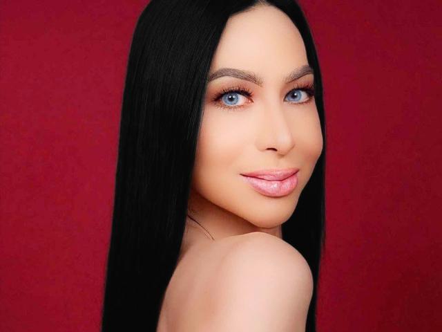 SexyTopHotMistress with long black hair, blue eyes, and pink lips, looking over her shoulder with a slight smile, showing her bare shoulders and smooth skin.