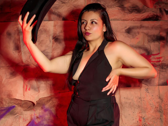 MargarettCooper with dark wet hair, black sleeveless top showing her tits, holding a black cloth, red and purple light on her, hand on hip, confident expression.