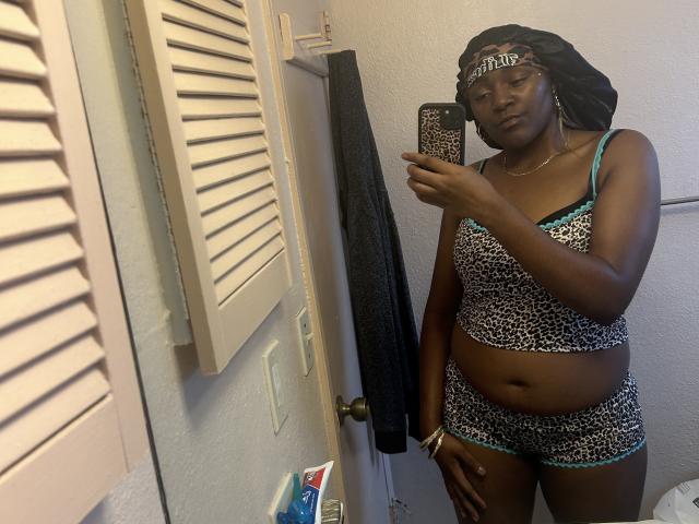 HoneyMakeMeCum with dark skin, wearing leopard print bra and shorts, black headwrap, holding phone, mirror selfie, showing small tits, flat ass, belly button, and confident expression.