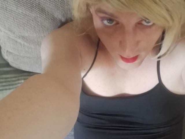 ZackaSissy20-hot with blonde hair, red lipstick, and black spaghetti strap top, looking up with a slight smile, showing a fair-skinned chest and arm.
