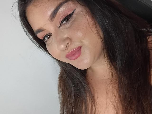 PattyHot69 has long brown hair, pink eyeliner, and glossy pink lips. She's smiling with a slightly tilted head, showing a shiny, clear complexion. Her tits are not visible.