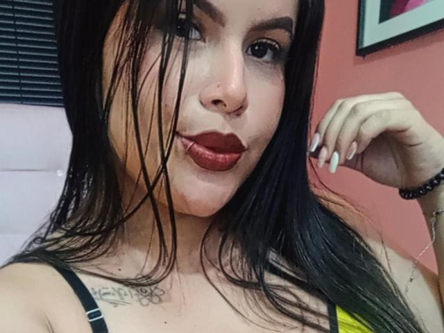 PlayfulCurvy with wet black hair, red lipstick, and a nose ring, showing off her tits with a tattoo just below. She's smirking, with one hand near her face.