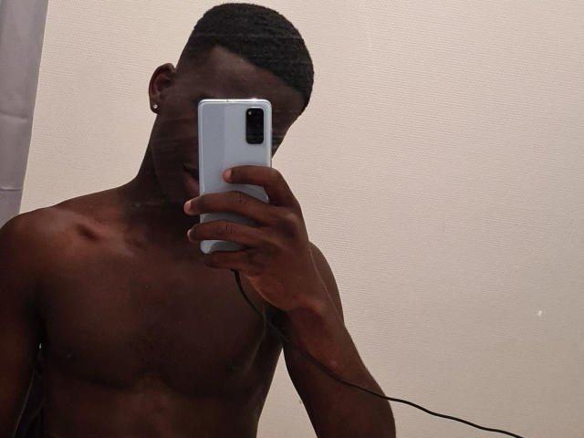ChrisHotS, senza camicia, con la pelle scura, capelli corti, che tiene un telefono davanti al viso, mostrando una parte superiore del corpo tonica con le costole visibili, in un selfie allo specchio..