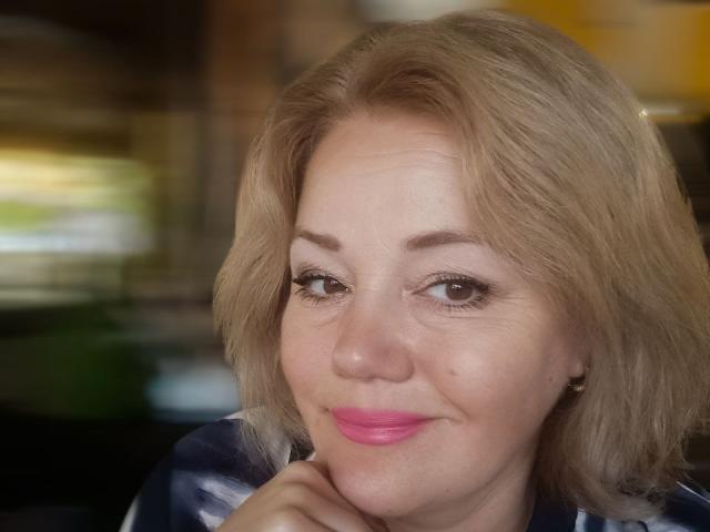 AlliRain has blonde hair, pink lipstick, and a slight smile. Her brown eyes are half-open, and she's resting her chin on her hand. Her tits are small.