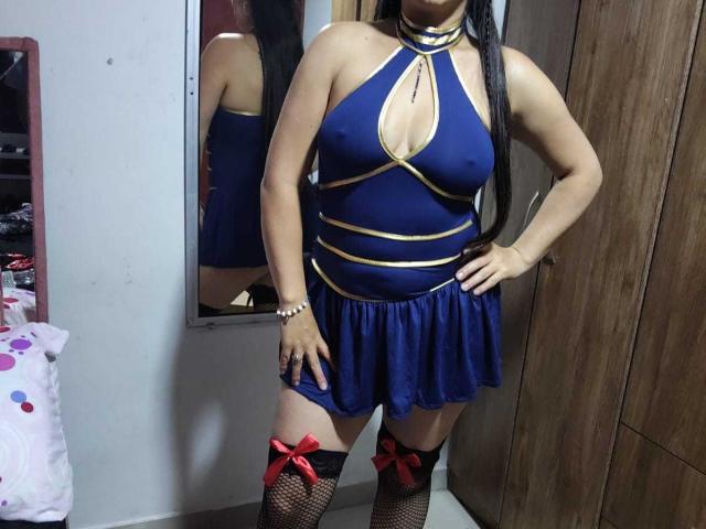 VenusSweetPalmer in a blue halter dress with gold straps, showing her tits, black fishnet stockings with red bows, long black hair, and a pearl bracelet.