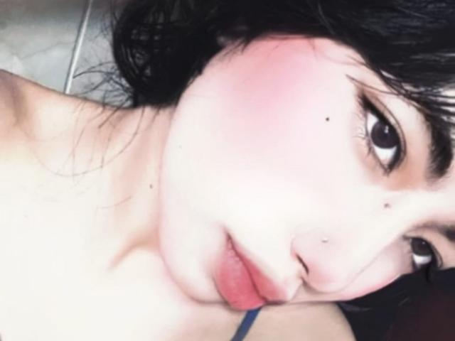 BrigidTerri's face with pink cheeks, dark wet hair, brown eyes, and nose piercings, showing slightly parted red lips, and a small beauty mark near her right eye.